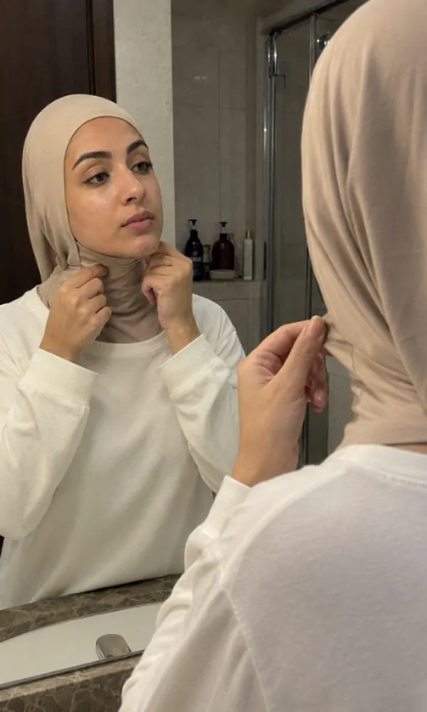 Woman adjusting underscarf neckline coverage in front of mirror