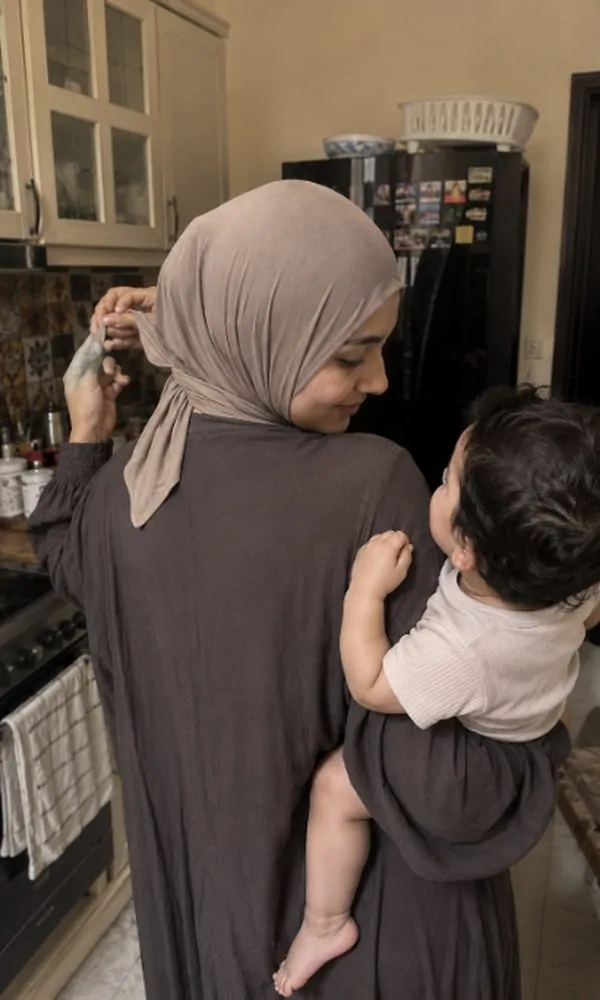 Woman tying underscarf closure while holding her baby